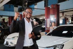 Smiling man holding a clipboard in an auto repair shop