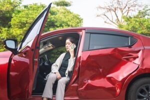Woman on the phone inside her damaged red car after a collision
