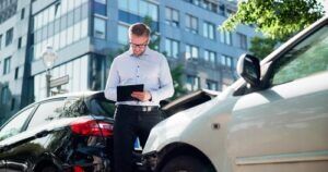 Man filling out an accident report beside two damaged cars