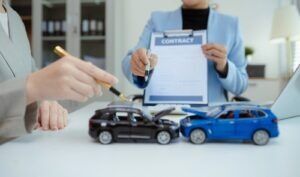 Car accident claim being signed next to two toy cars