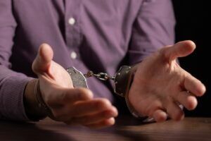 The hands of a handcuffed man at an interrogation table. What should I do if I am charged with murder in Arizona?