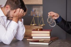 Worried man at a desk as handcuffs are held out beside him