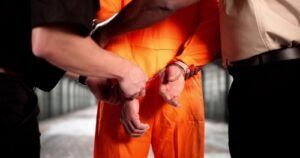 Handcuffed person in an orange jumpsuit being escorted