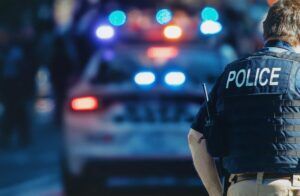 Police officer standing beside patrol car with emergency lights, domestic violence case context