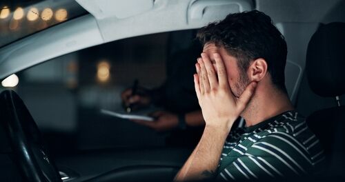 Driver seated in car during traffic stop, looking anxiously toward officer outside