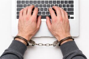 A handcuffed individual at a laptop facing internet sex offense charges in Phoenix.