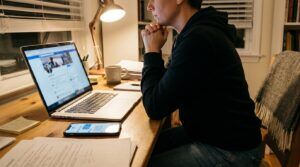 person at desk viewing social media profile on laptop with documents nearby