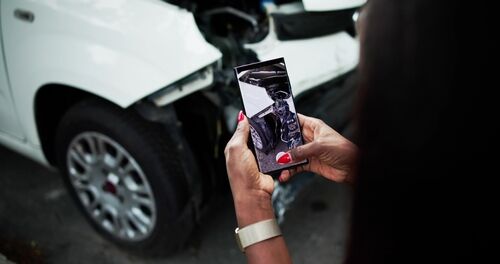 person photographing severely damaged vehicle with smartphone after collision