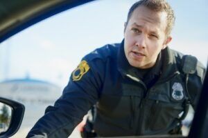Police officer leaning into car window during roadside traffic stop conversation