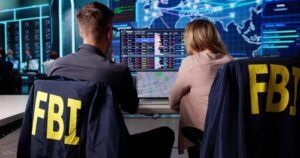 Two people at computer monitors with FBI jackets in surveillance operations room